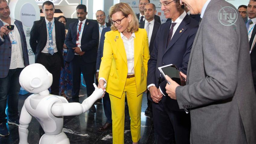 Doreen shakes hands with a robot amidst a group of people who surround her and take photos