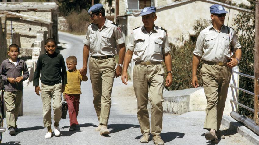 Three male soldiers are walking with children while patrolling the streets. 