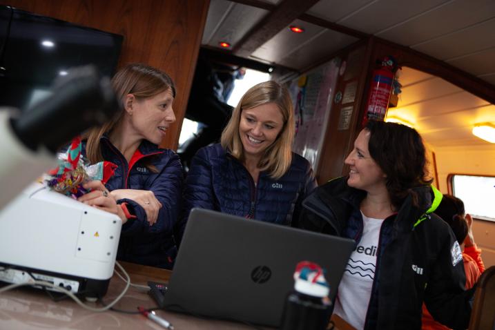 Emily Penn (centre) and colleagues analyse samples of ocean plastics aboard the sailing vessel TravelEdge using a Fourier transform infrared (FTIR) machine, 2019. eXXpedition/Sophie Bolesworth