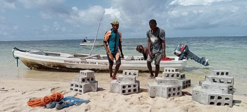 Des hommes sur une plage embarque des parpaings sur une bateau