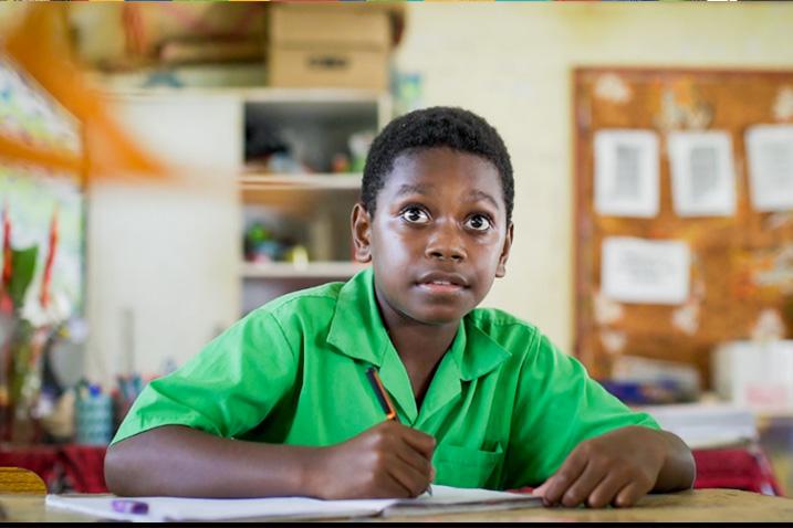 A young student looks up from his work in a classroom 