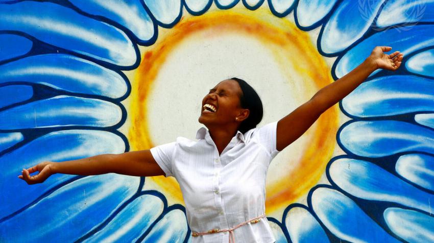 Une femme pose devant un graffiti représentant le soleil à l’occasion de la célébration de la Journée mondiale de la santé mentale. Dili, au Timor-Leste. Photo ONU/Martine Perret