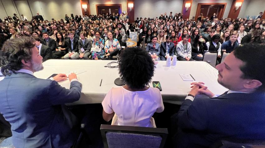 Three delegates with the crowd of Model UN participants in front of them.