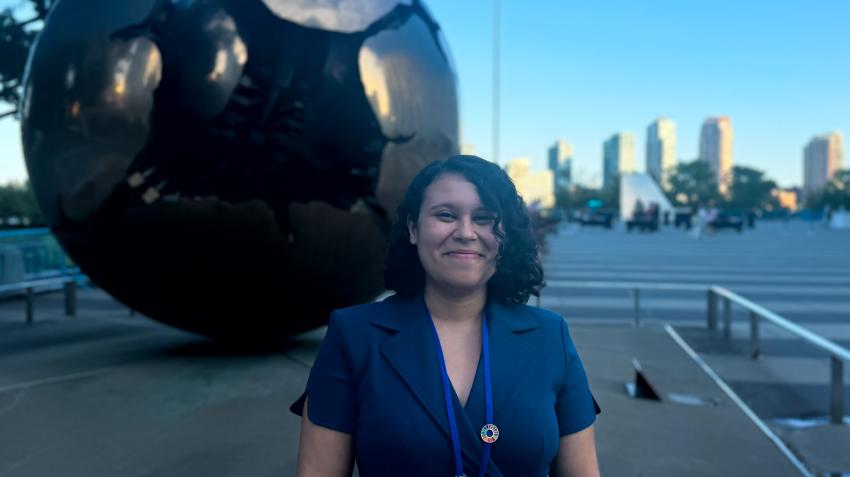 A young woman stands in front of a statue depicting a sphere inside a sphere