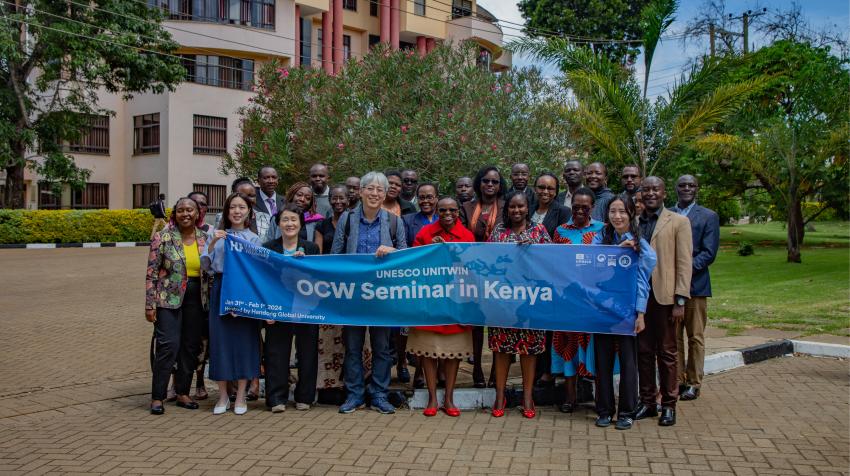 A large group of people stand in front of a banner which reads: UNESCO UNITWIN OCW Seminar in Kenya