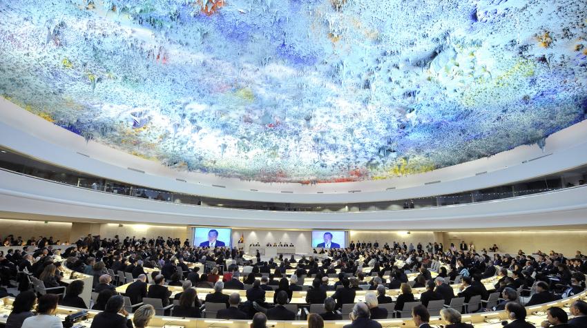 Eye-level view of a large circular conference room with a colorful ceiling containing dozens of seated individuals