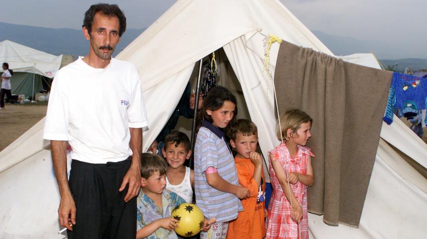 A refugee family is standing in front of a white tent in the refugee camp for Albanian refugees from Kosovo.