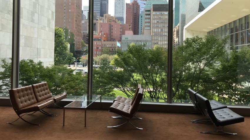 Zoomed in resting area facing outside of the building, with four cushioned seats and glass coffee table in the middle. 