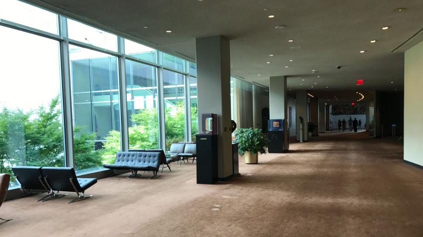 A long carpeted hallway with a resting area beside a glass wall that faces the building's outside.  