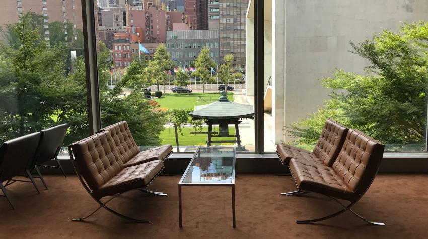 Zoomed in resting area facing outside of the building, with four cushioned seats and glass coffee table in the middle. 