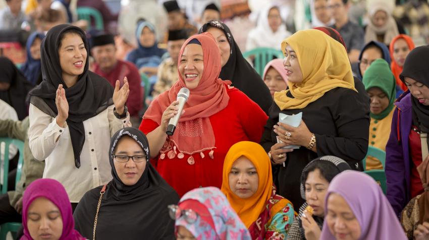 Woman holding mic, participating in UN Women hosted discussion on how women contribute to peace in their community