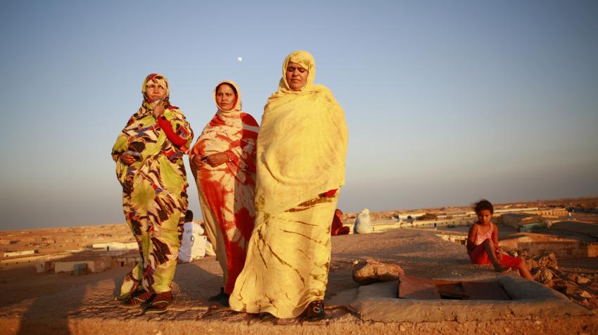Three women are walking at sunset near a refugee camp in the Western Sahara area. 