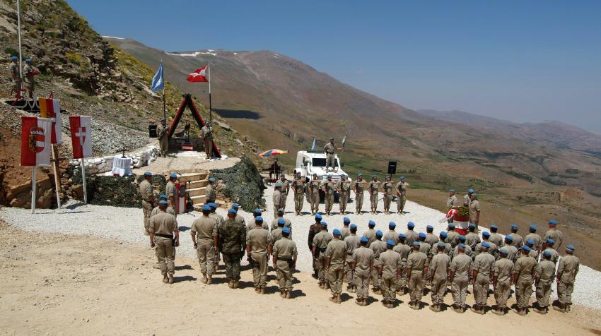 Peacekeepers are gathered at a memorial site for the mission's 1st Company Australian contingent. Three soldiers are surrounding a memorial.