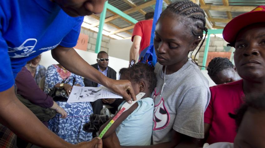 A child's arm is being measured by a staff member at a clinic in Haiti. 