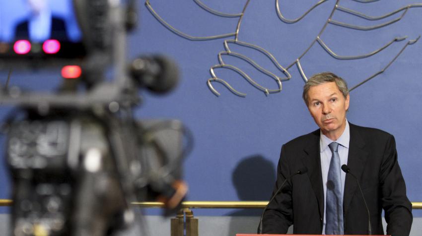 View of camera filming a man speaking in front of the lounge wall with blue artwork.