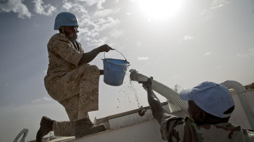 Male figure from the Ivoirian Transport Company is delivering drinkable water through a hose to a male peacekeeper holding a blue bucket. 