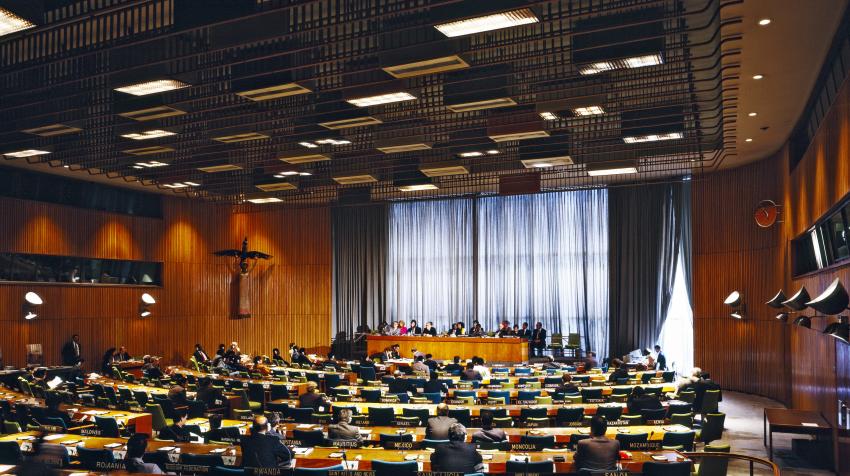 View of the Trusteeship Council from the right side of the chamber, with the wall statue in the front, windows covered with half-transparent curtains in the front, and several rows of seats.  