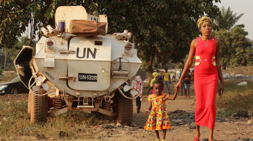 Mother and child are standing in front of a UN-engraved vehicle, celebrating a youth peace week.