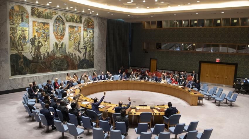 View of the Security Council chamber from the left side of the room, with a round table for delegations and a mural of a pheonix on the wall. 