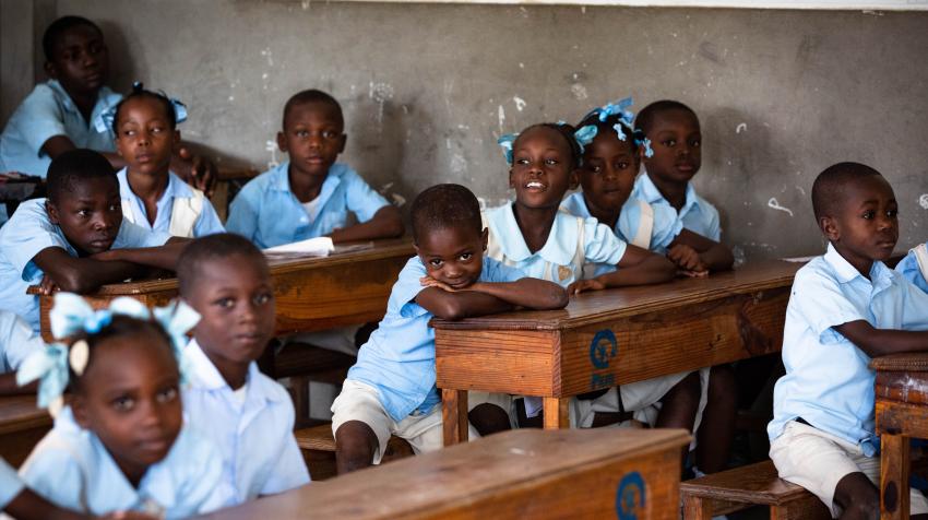 Children in school uniforms sitting on school desks. 