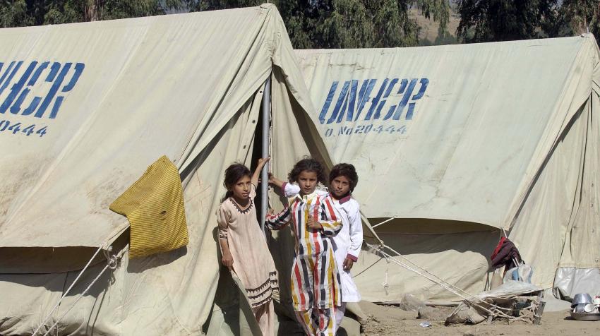 Three girls are in front of a tent set up by the office of the United Nations High Commissioner for Refugees. 