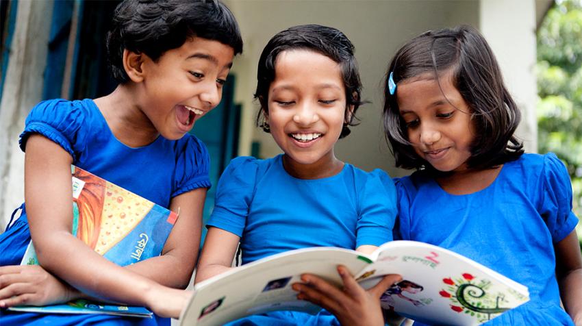 Three classmates in Bangladesh read together from a children’s book provided by the non-profit organization Room to Read.