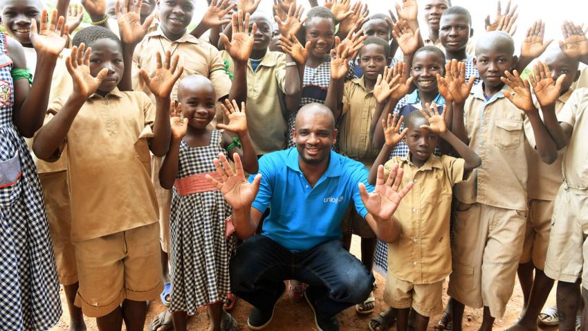 Aboubacar is crouching amidst a group of children. All are holding their hands up.