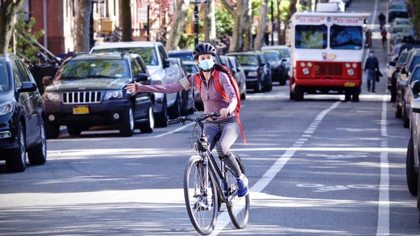 A bicyclist wearing a mask signals while making a turn.