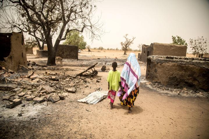 A woman and her daughter walk past the remains of destroyed homes during the March 2019 attack on Ogossagou village by armed Dogon men in which over 150 civilians were killed. 