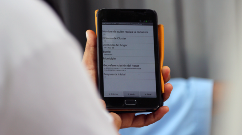 Une main tient un telephone portable qui affiche une application pour le tracage de contacts.