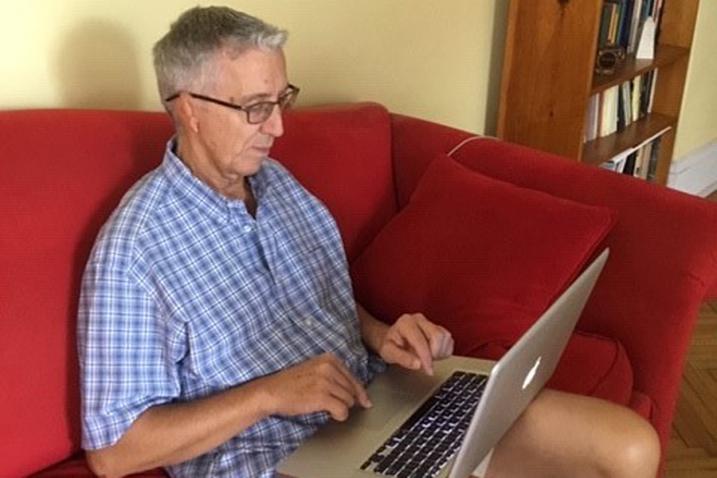 Man sitting in a couch with a laptop on his lap. 