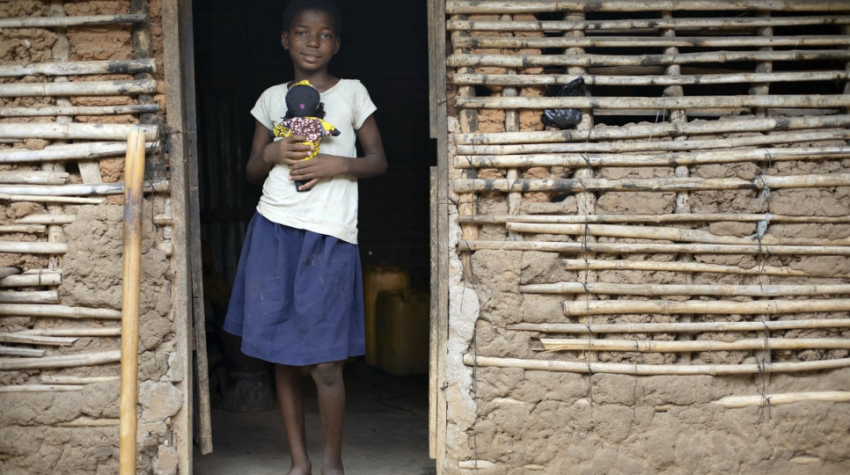 Congolese refugee Nadine, 9, holds one of the dolls made by her mother, Kituza, in Maratane camp, Mozambique. girl in doorway holds doll