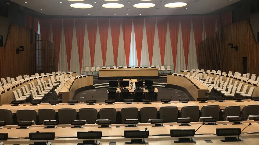 Zoomed in view of the ECOSOC chamber with seats arranged around the room and wall decoration of interchanging red and white triangles. 