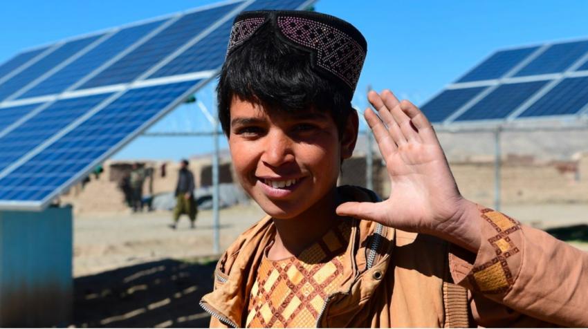 A boy waves in front of solar panels that provide electricity to pump water, in Herat, western Afghanistan.