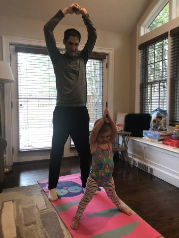 Un padre practica yoga en casa junto a su hija. 