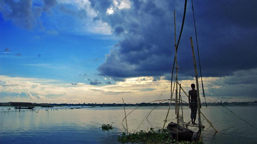 A fisherman at dusk stands above the water