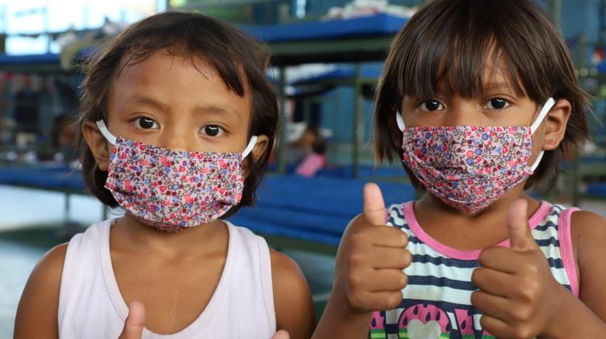 children with masks showing thumbs up