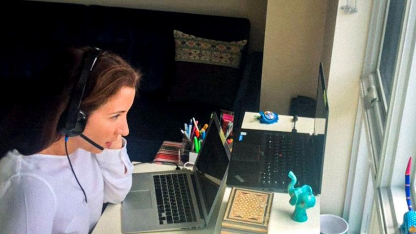 Woman wearing a headset with a microphone sits in front of two laptops.