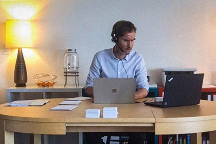 Man with a headset and microphone sits in front of two laptops. 