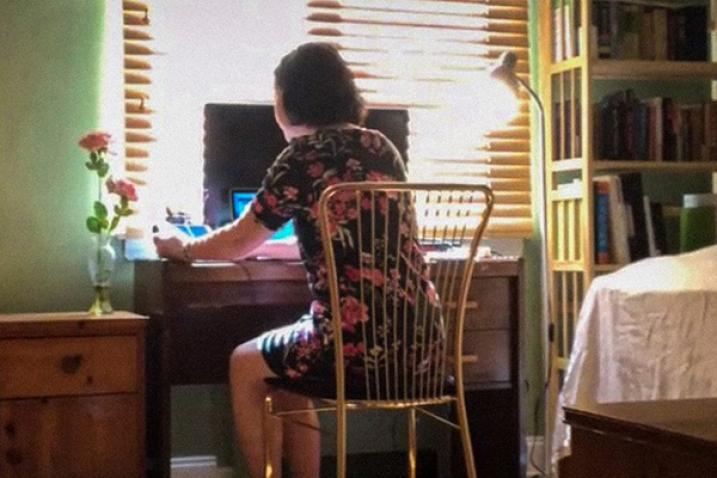 Back of a woman working from a tablet with another laptop and desktop computer in front of her.