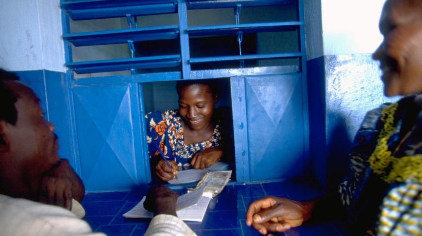 Une employee dans un kiosque d'envoi de fonds rempli des papiers pendant qu'un couple attendent.