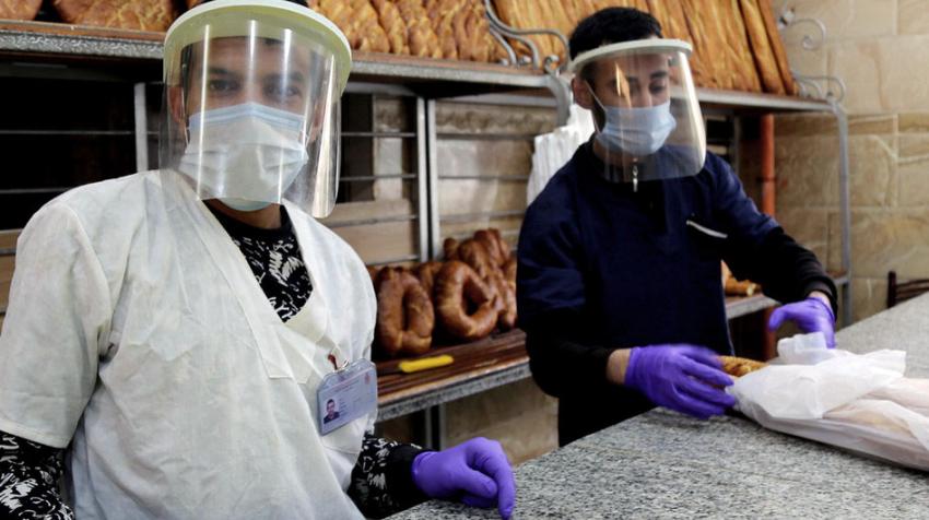 Deux vendeurs protégés par des écrans faciaux vendent du pain dans une boulangerie.