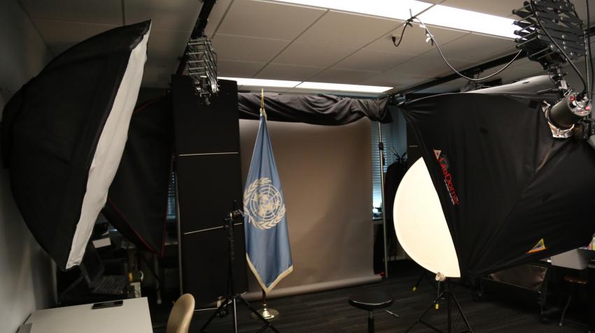 Entrance view of a studio with lighting equipment, a UN flag, and a set of different background screens. 