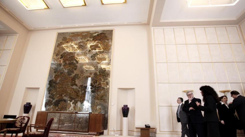 View of the lounge with white, square-tiled walls, artwork on the wall's center, and lavishly decorated carpet. 