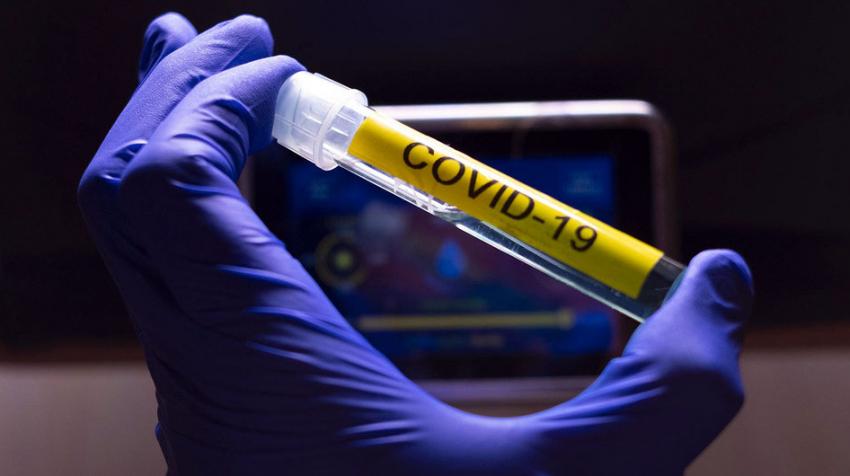Une main tient une eprouvette de laboratoire etiquettee COVID-19