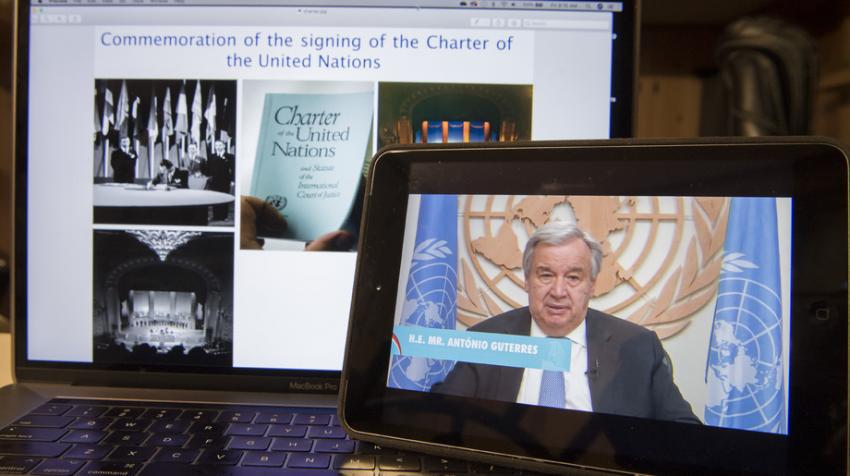 Secretary-General António Guterres on screen in front of bigger screen with UN Charter photos