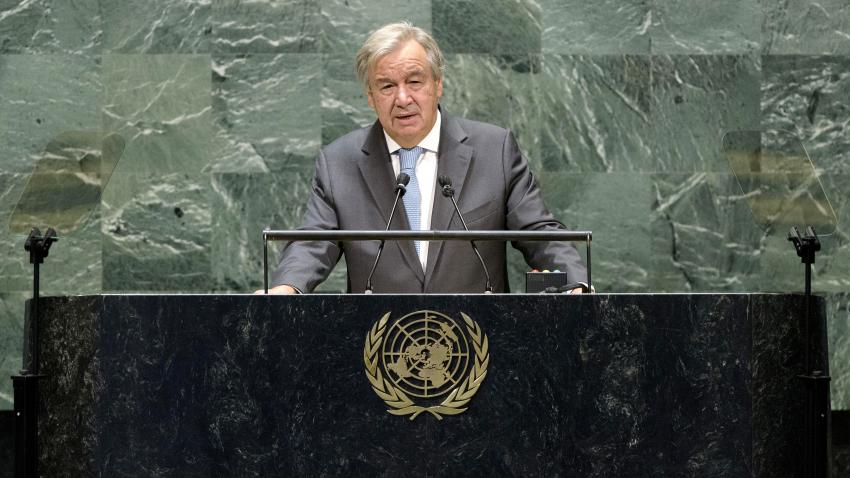  El Secretario General hablando en un podio de mármol negro con un emblema dorado de la ONU.