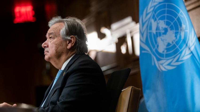 Le Secrétaire général regarde devant lui, à côté du drapeau de l'ONU.