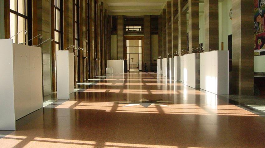 Long hallway with brick-colored floor with brown pillars on both sides of the hallway. 