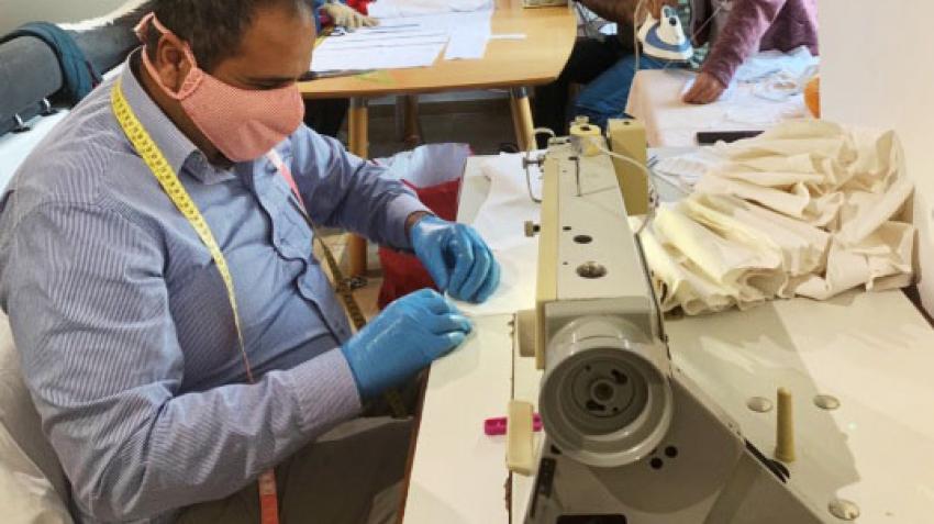 Iraqi refugee Mohammed Alhashimi sews masks in Luxembourg. He is seated at a sewing machine, wearing a face mask.